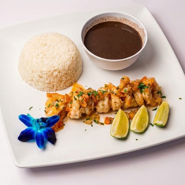 Shrimp with rice, black beans, lime wedges, and a blue orchid on a white plate.