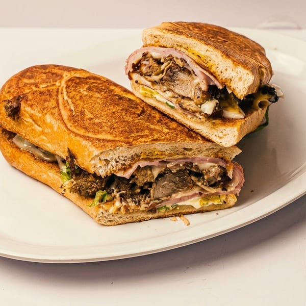 Toasted Cuban sandwich cut in half, revealing pork, ham, cheese, and mustard on a white plate.