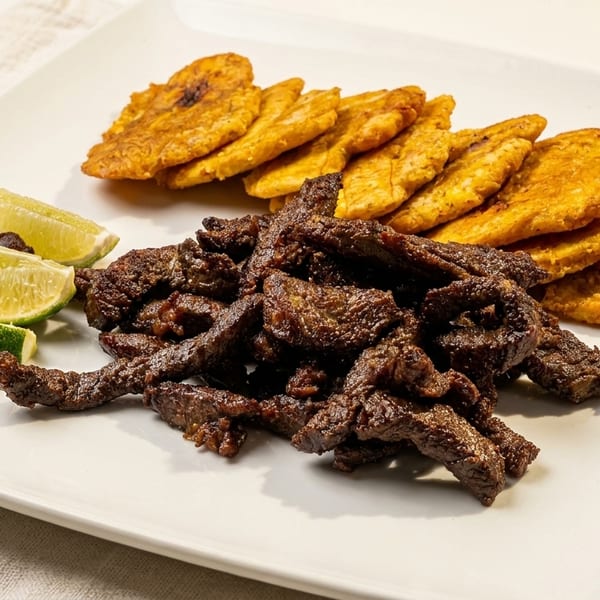Fried meat strips, golden plantains, and fresh lime wedges on a white plate.